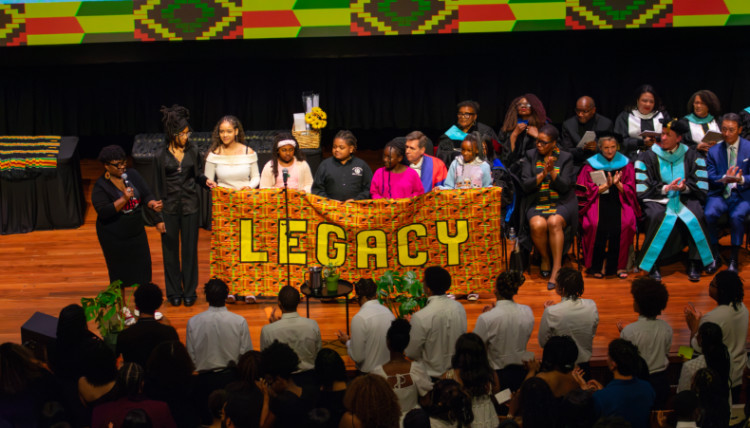 Students on stage hold a banner that reads "Legacy"