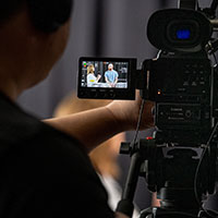 Videographer looking through a camera mounted screen at a person.