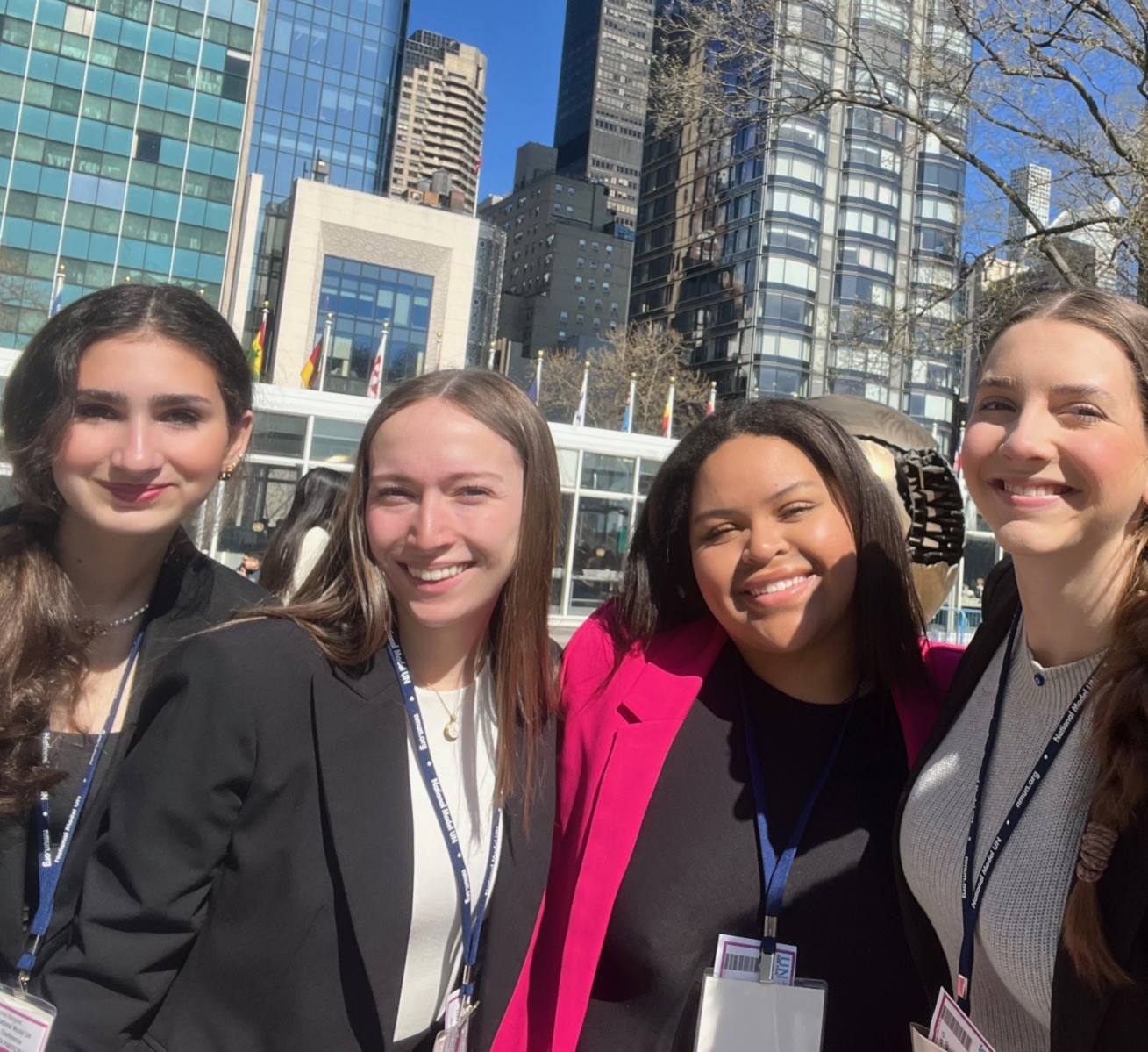 Gonzaga University Model United Nations delegates standing outside the United Nations Headquarters in New York City, wearing professional attire and conference badges, with modern skyscrapers and international flags in the background.