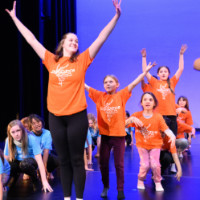 Children following an adult leader in a line dancing.