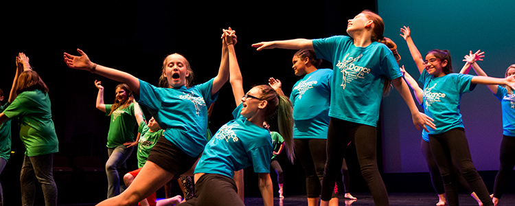 Several childen in matching blue shirts dance as a group.