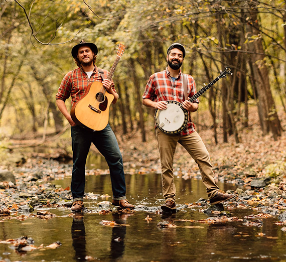 The Okee Dokee Brothers standing in the woods with their instruments.