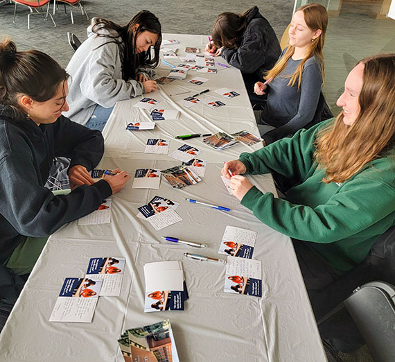college women seated at a table covered in postcards