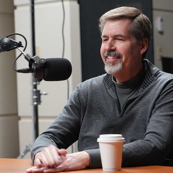 Thayne McCulloh behind a podcast microphone and a coffee cup in the foreground.