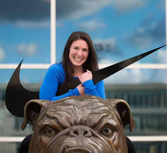Alumna Sara Wedland ('15 ’15, B.Ed. Sport Management, B.A. Applied Communications) holding Nike logo on top of bronze Spike the bulldog statue