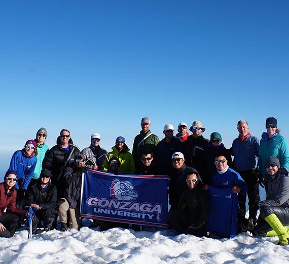 Gonzaga Students holding up Gonzaga flag at the top of Mt Adams posing for a group photo