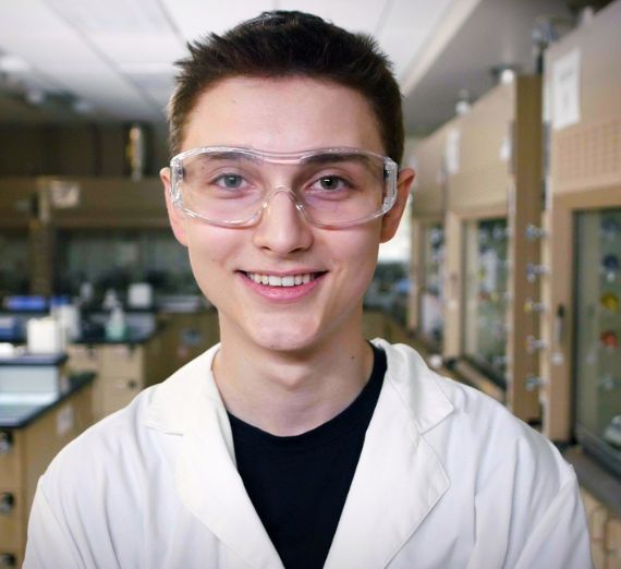 A student in lab goggles and a white lab coat.