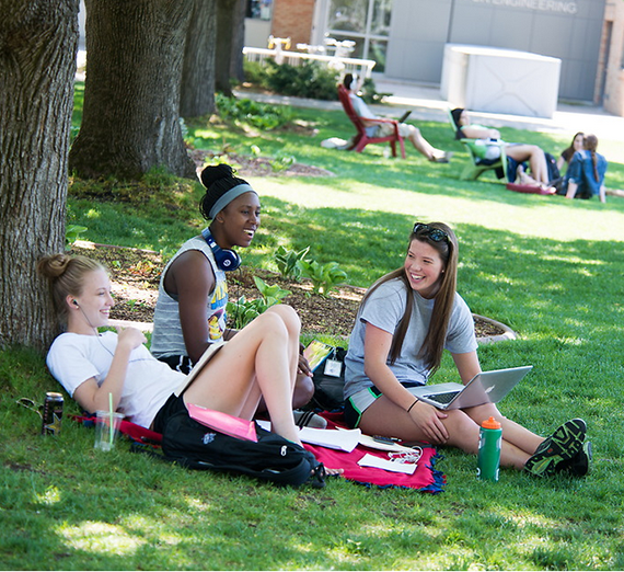 Three students sit on a lawn