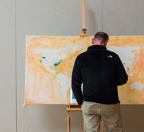 Person facing a large world map on an easel, marked with blue and red locations.