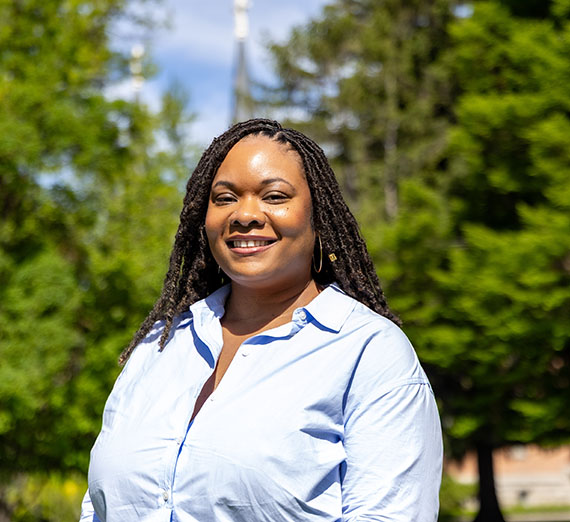 Women wearing blue button up standing with trees and campus behind her 