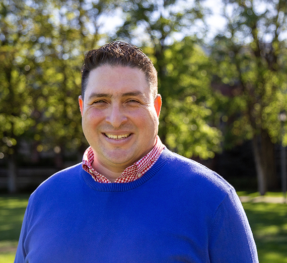 Man in blue sweater with green trees in the background 