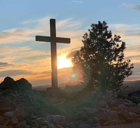 A cross and a pine tree at sunset