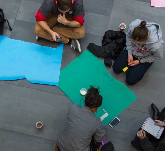 Students sitting on sidewalk with poster paper and markers