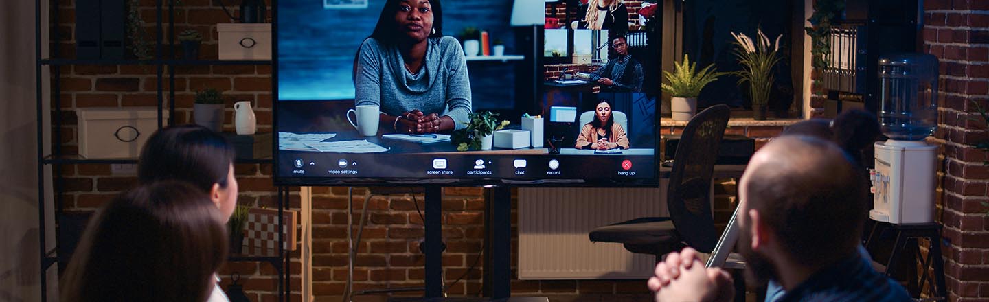 Group of people in room at a table meeting with more people on a video conference call