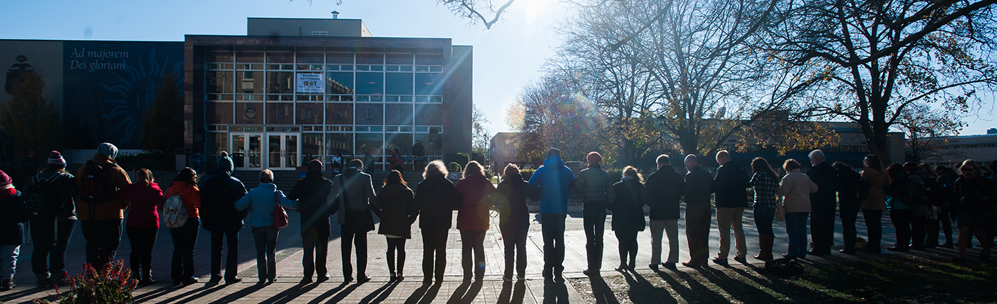 Silhouette of students locking arms in unity with sun shining brightly in the sky.