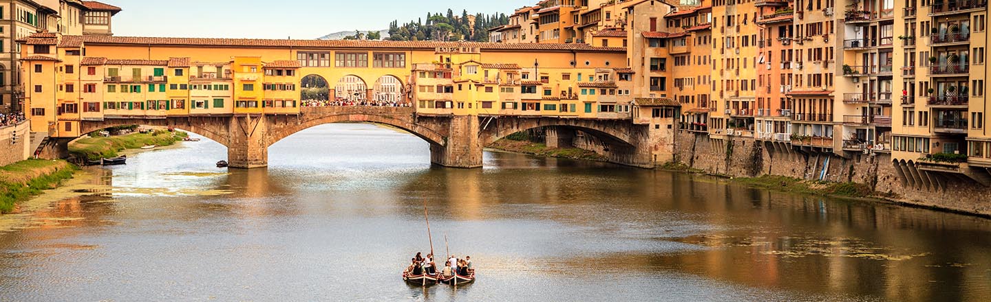 A river with two boats in front of a bridge at Ponte Vecchio, Florence