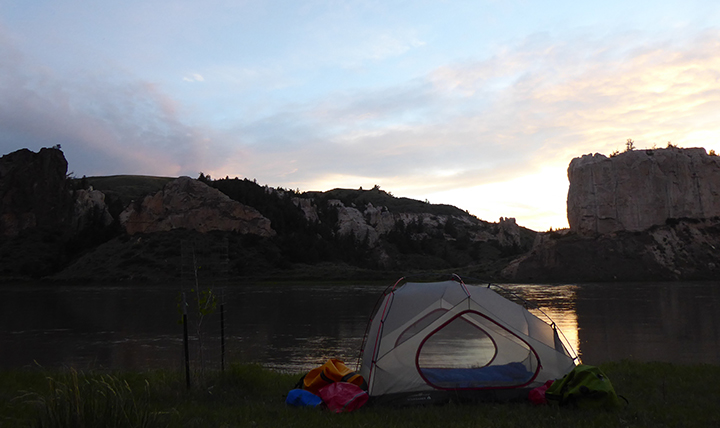 A tent sits next to the river as the sun sets 