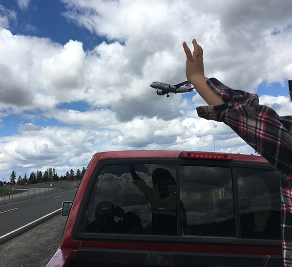 Young boy waves hands at clouds in sky