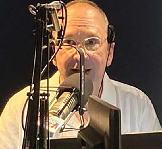 Gregg Hersholt sits behind a radio microphone.