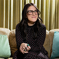 Leah sits on a couch with teal pillows.
