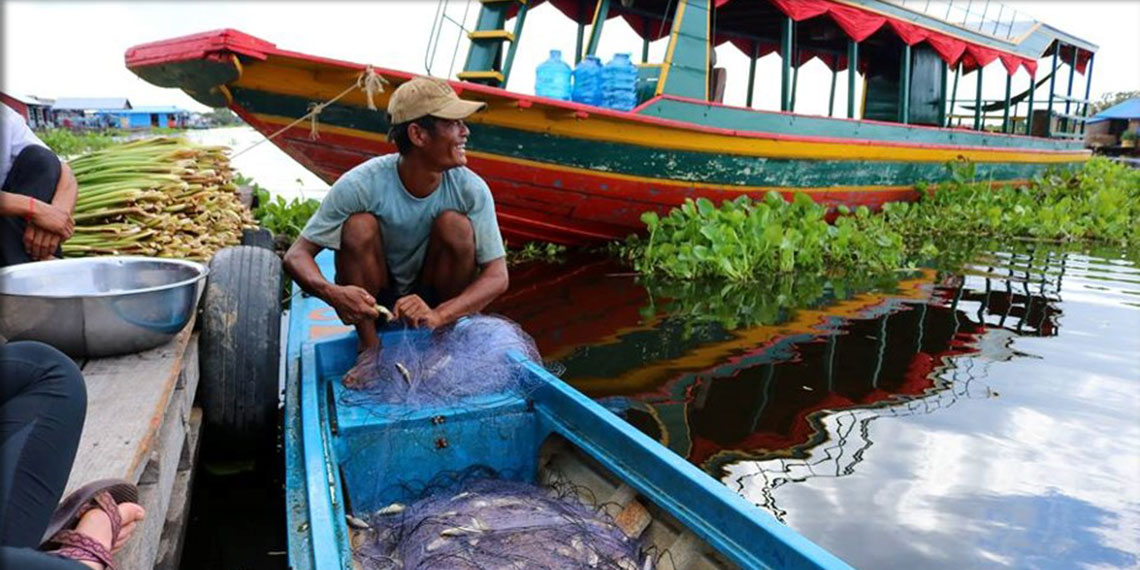 A fisherman in Cambodia crouches on the end of his boat