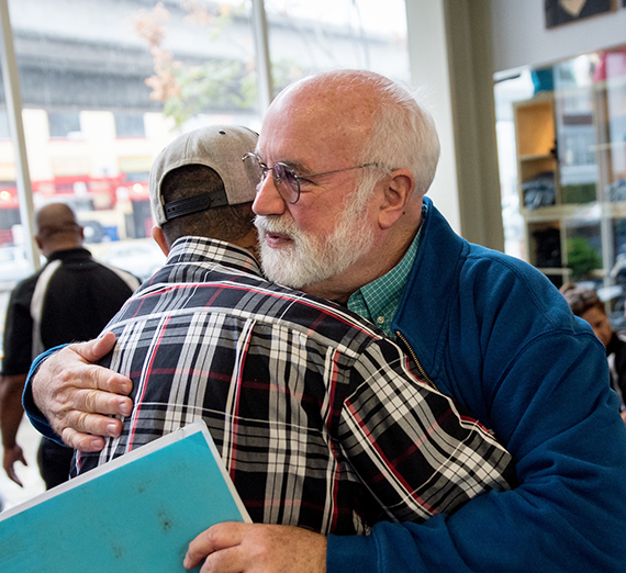 Father Greg Boyle hugs a man wearing a baseball cap