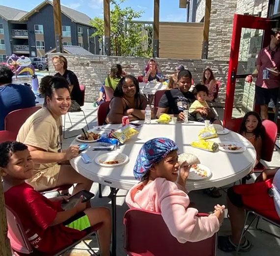 Children and adults sit around a round table enjoying a meal