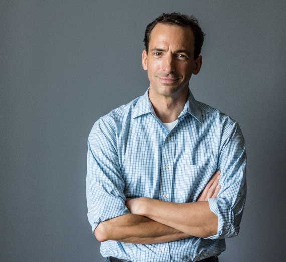 Paul Tough standing with his arms crossed, looking at camera