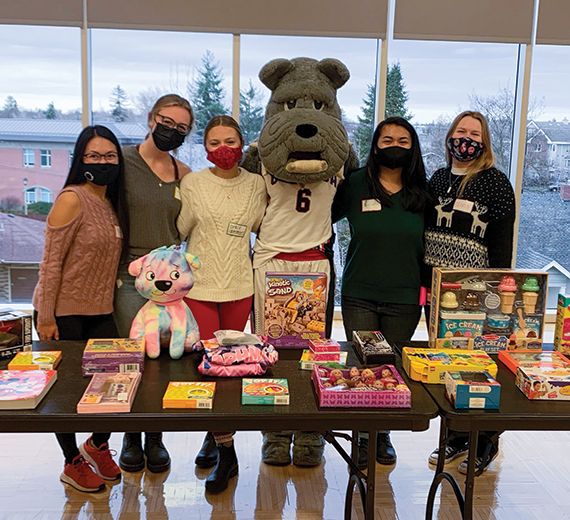 5 college students standing behind tables of gifts with Spike the Gonzaga mascot. 