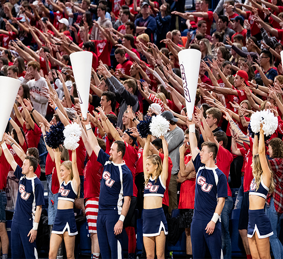 A faraway shot of a group of cheerleaders and students watch a basketball game.