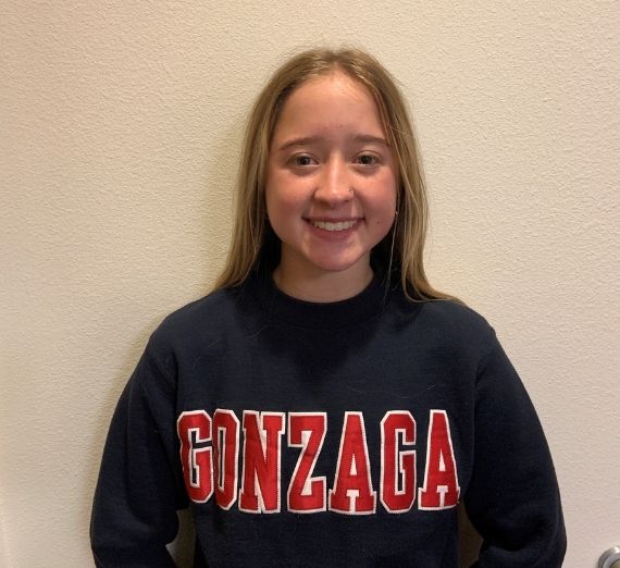 Jade, a current student, smiling against a blank wall. She is wearing a navy crewneck sweatshirt with GONZAGA in red letters.