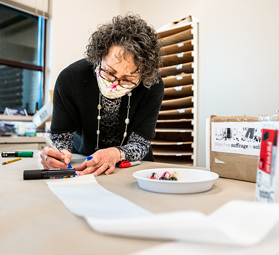 woman decorates sash with colorful markers