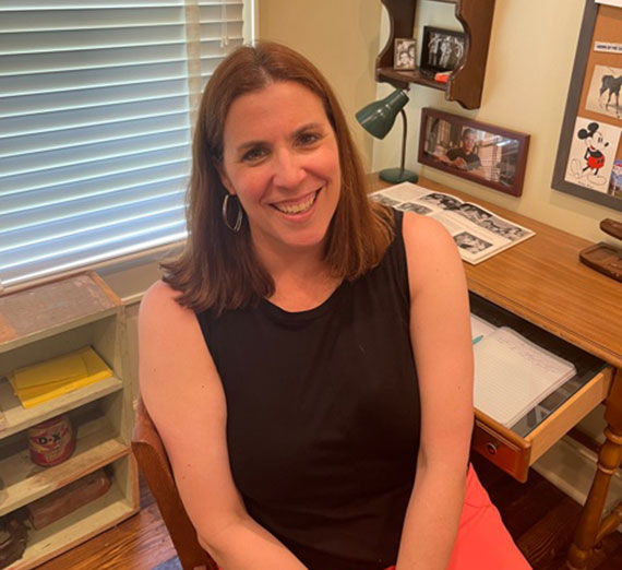 Professor Ann Ciasullo sits in front of a small wooden desk at the Outsiders House Museum