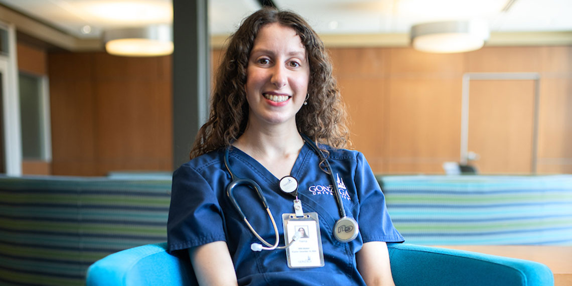 Sierra Martinsen sits in a chair wearing medical scrubs