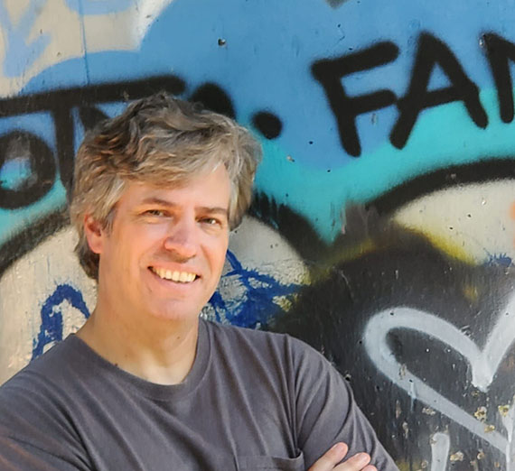 Brad Bunn stands in front of a wall with spray paint art 