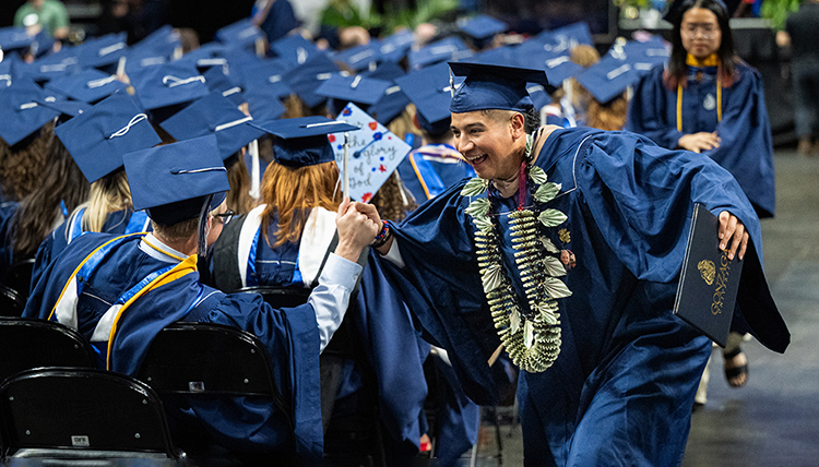 A graduate high-fives his peers as he runs down the aisle at commencement