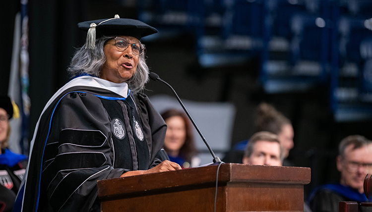 A woman in graduation regalia speaks at a podium