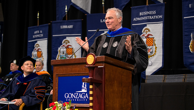A man speaks at a podium while another man looks on