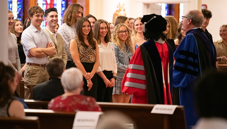 A group of students stands in front of people in graduation robes