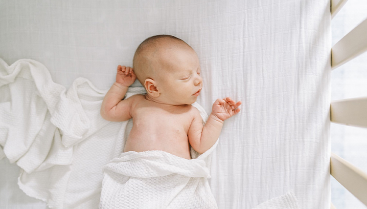 A newborn baby takes a nap in white sheets.