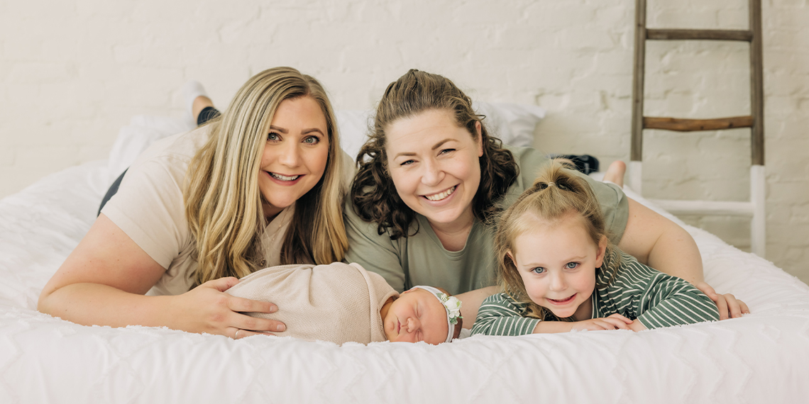 Two women smiling with their child and newborn baby.