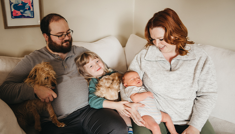 A couple holds their kids and dog while sitting on a couch.