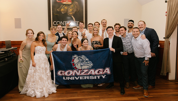 A group of people pose with a Gonzaga flag at a wedding.