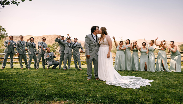 A couple kisses in front of their wedding party.