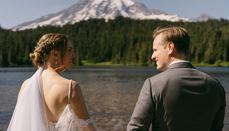 Two people smile at each other in front of a mountain.