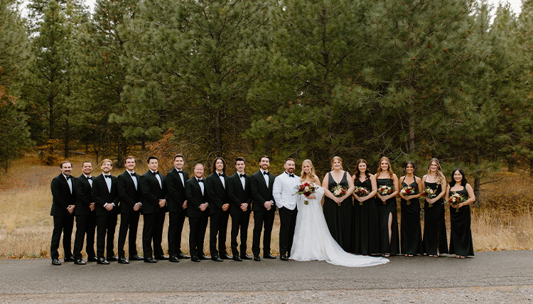 A wedding party wearing black and white pose in a line.