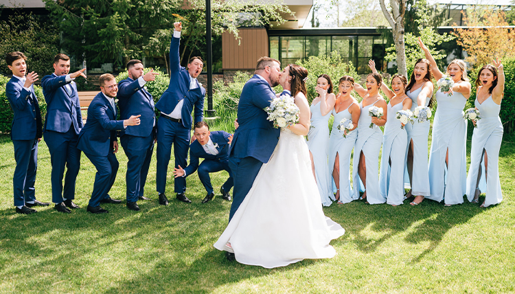 A bride and groom kiss in front of their wedding party.