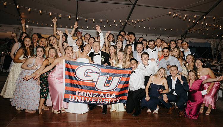 A big group of people smile and pose with a Gonzaga flag.