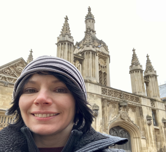 Melody Alsaker in beanie and jacket poses in front of medieval building.