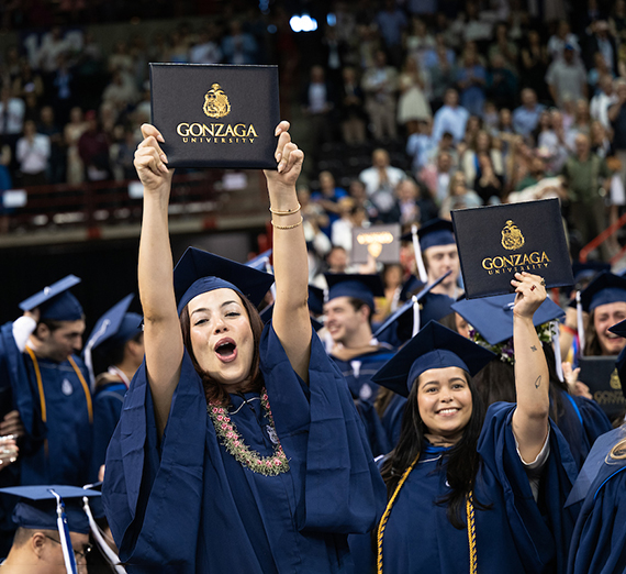 A woman in graduation regalia holds up her degree